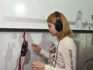 Student interacting with a physical prototype which is a mask with LED lights and wearing headphones at IDM showcase 2017